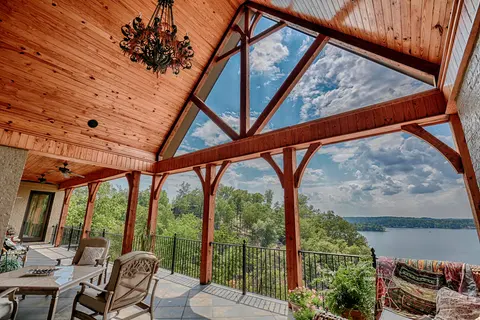Covered timber-framed terrace with a wood-plank ceiling and open gable trusses overlooking a lake