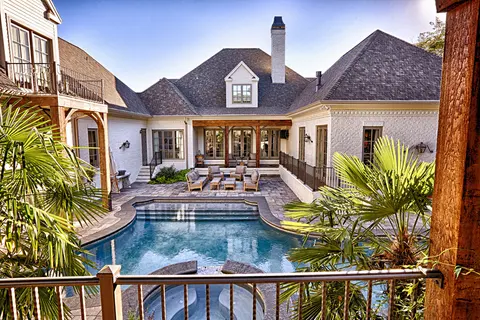 View over a courtyard swimming pool toward the back of a white brick home with a covered porch