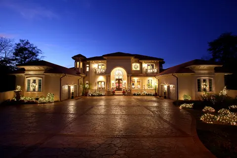 Mediterranean-style home at twilight with lit windows, a tile roof and a stamped-concrete motor court