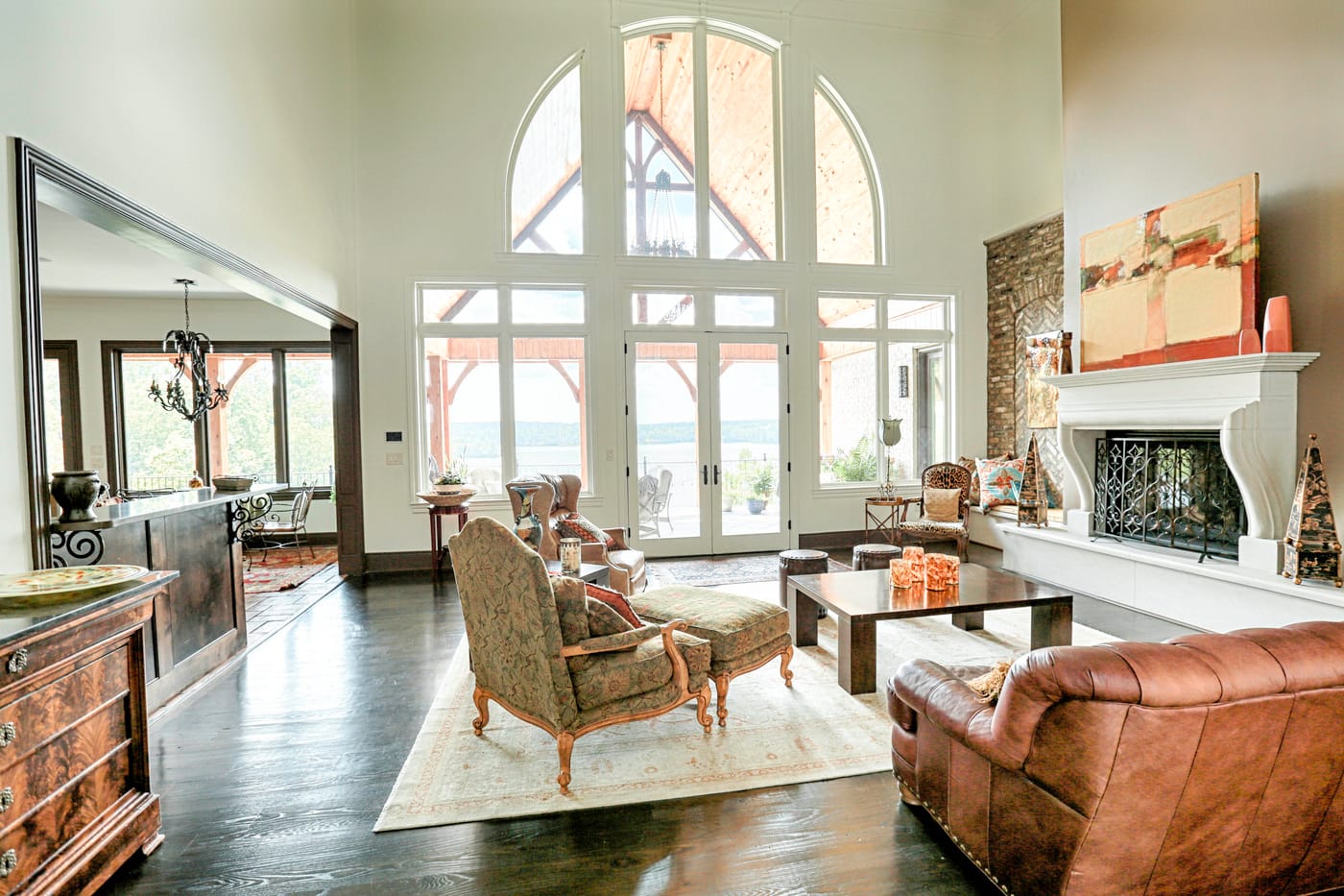 Great room with arched two-story windows, a carved white fireplace, dark hardwood floors and leather seating