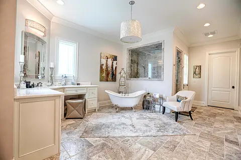 Bathroom with a clawfoot tub, cream vanity and dressing table, a beaded pendant light and stone tile floor