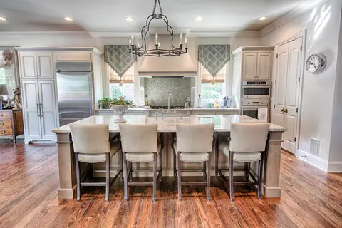 Kitchen island with four upholstered stools facing the range, with cream cabinets, an iron chandelier and wood floors