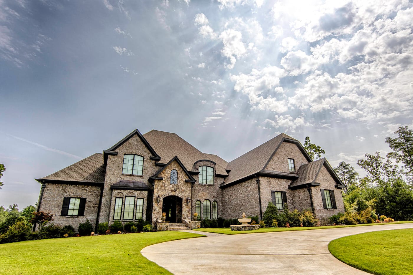 Stone home with steep gabled roofs, an arched front entry and a curved concrete driveway