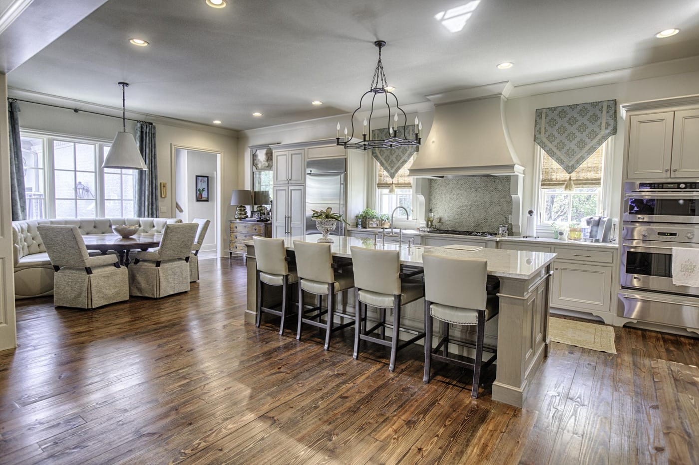 Open kitchen and breakfast area with cream cabinets, a large island with four upholstered stools, an iron chandelier and wide-plank wood floors