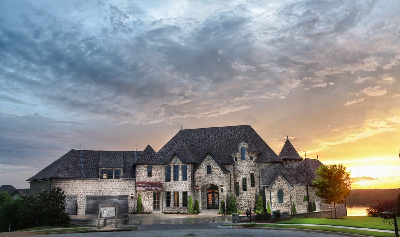 Stone home with steep rooflines and turrets at sunset, with water visible beyond