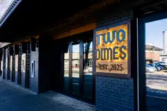 Angled view of the Two Dimes entrance with black brick, glazed doors, timber soffit and illuminated sign
