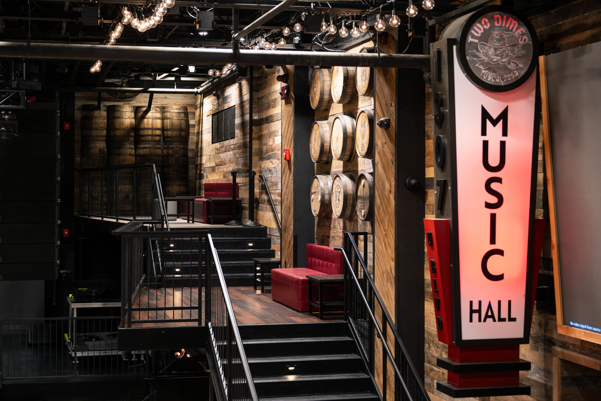 Finished raised seating at Two Dimes with timber floors, red benches, stairs, black metal rails and a Music Hall sign