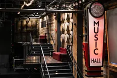 Finished raised seating at Two Dimes with timber floors, red benches, stairs, black metal rails and a Music Hall sign
